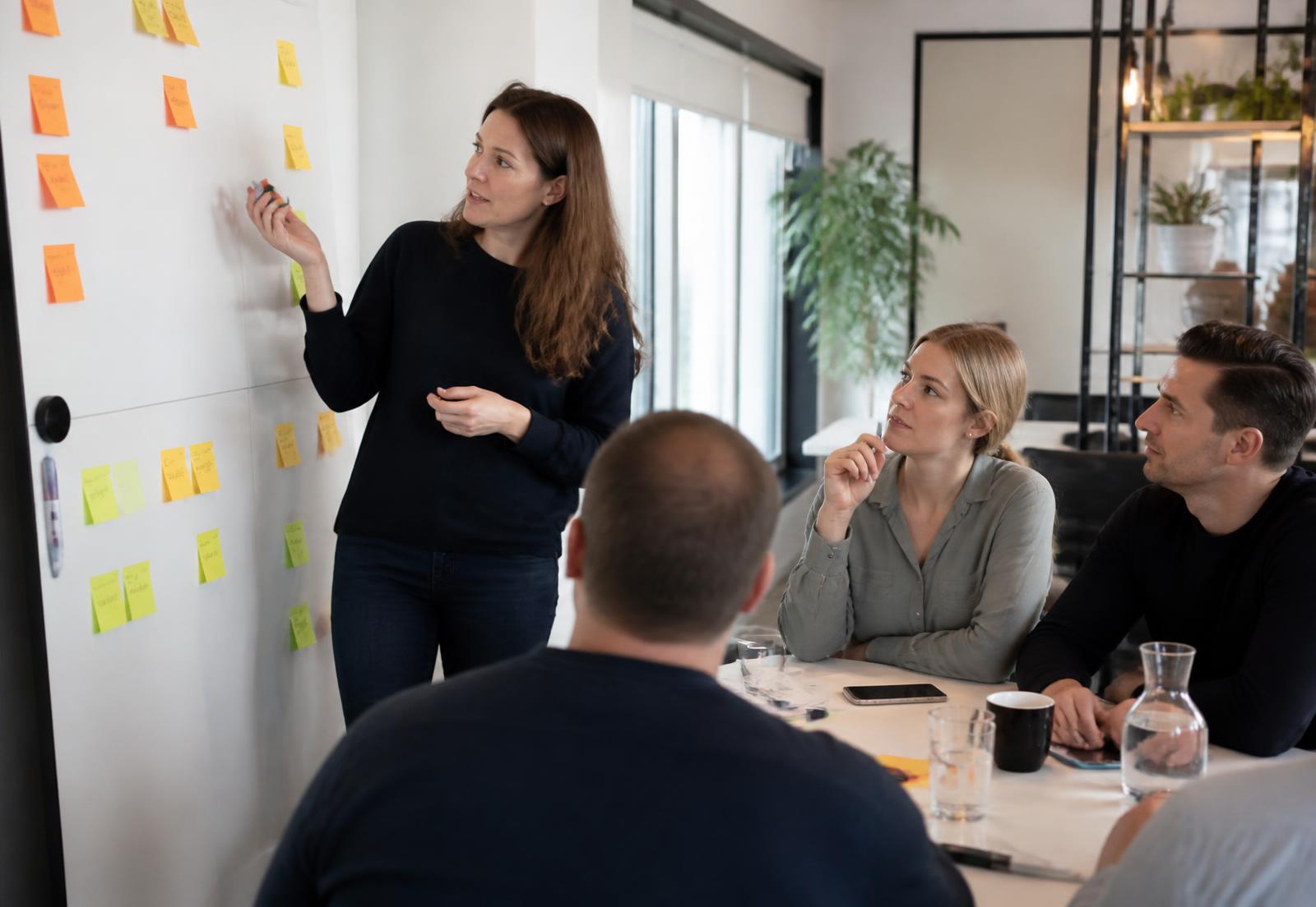 Scrum Master faciliteert een planningssessie met haar team bij een bord met post-its